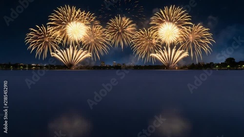 Golden fireworks exploding over lake at night. Festive pyrotechnic show with rocket launch and bright bursts reflecting on water.