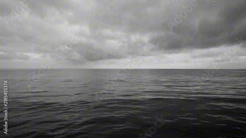 A vast, grey ocean under a dramatic, cloudy sky. The dark water reflects the ominous weather, creating a sense of solitude and immensity
