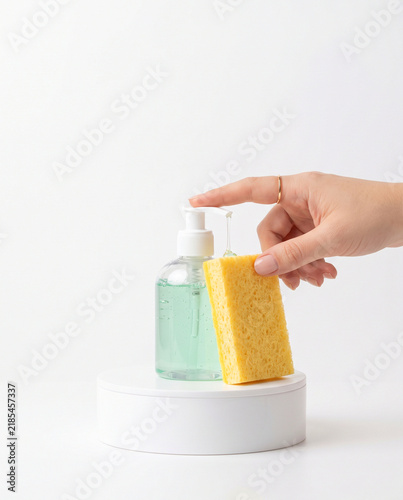 Hand Pumping Liquid Soap onto Yellow Sponge on White Podium
