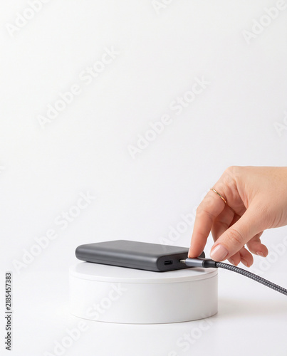 Hand Plugging USB-C Cable into Slim Power Bank on White Podium
