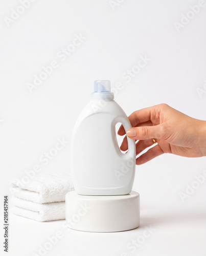 Hand Holding White Laundry Detergent Bottle with Towels on Podium
