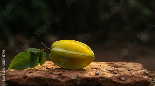Whole starfruit with leaf on terracotta slab with warm dramatic lighting and soft dark background