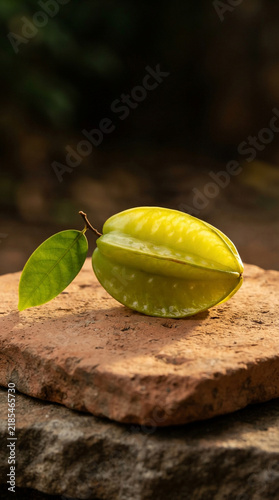 Starfruit with translucent waxy yellow-green ridges on raw terracotta clay with dramatic rim light