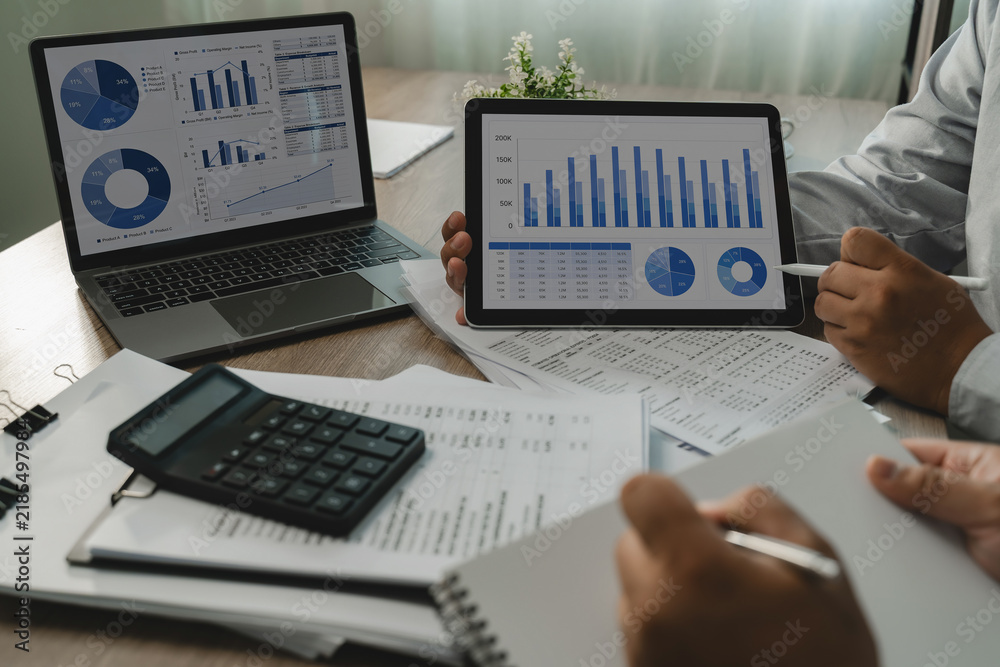 Obraz premium Business team reviews charts on a laptop and tablet beside printed reports and calculator, comparing figures and dashboard data for business analysis, reporting, and financial management.