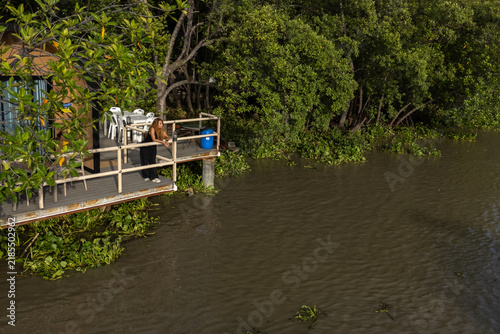 A woman stood on the balcony of a house by the river, which was surrounded by mangrove forest.