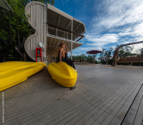 A woman sits on a yellow kayak on the riverbank.
