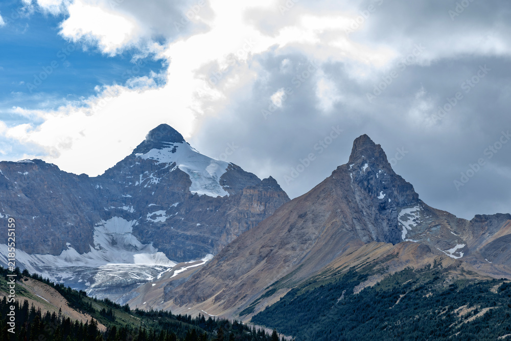 Obraz premium Majestic snow-capped mountains under a dramatic cloudy sky, Glacier Rd, Jasper, Canada