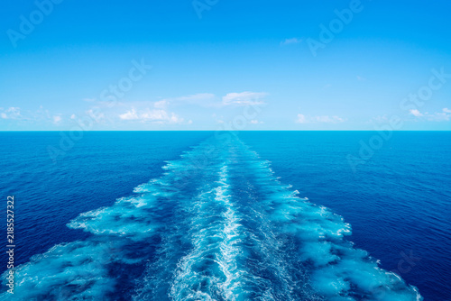 Water wake trail left by cruise ship in deep blue ocean under clear sky with copy space