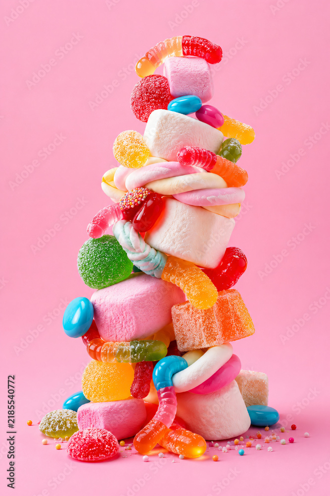 Fototapeta premium Colorful stacked pile of assorted gummy candies and marshmallows creating a sweet tower on a vibrant pink background