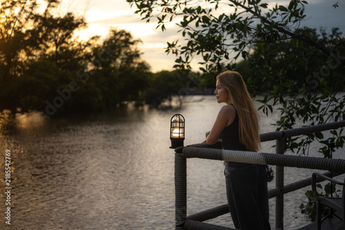 A long-haired Asian woman stands by the river in the evening.