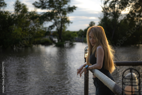 A long-haired Asian woman stands by the river in the evening.