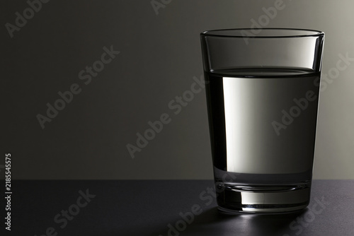 Glass of still water backlit dramatically on dark background, hydration and purity concept