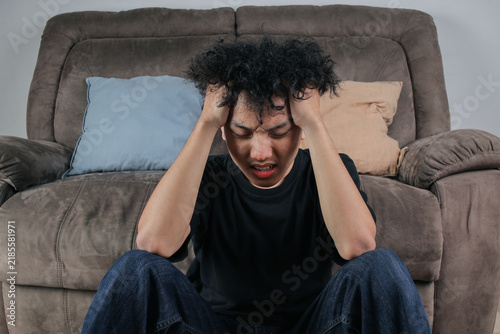Foto Stressed Young Asian Man Sitting On The Floor Holding His Head In Frustration In