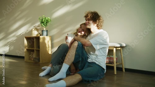 Couple sits on the wooden floor in a bright room with plants and natural light during the day while sharing laughter and conversation