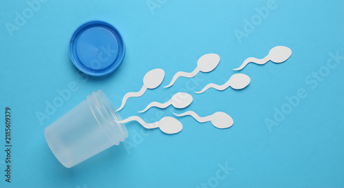 White papercut sperm cells emerging from a tilted sample collection container with its blue cap on a blue background.