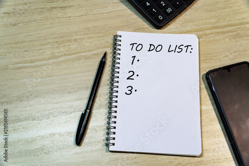 To Do List text on spiral notebook with pen, smartphone, and calculator on wooden office desk background. Planning and task management concept.