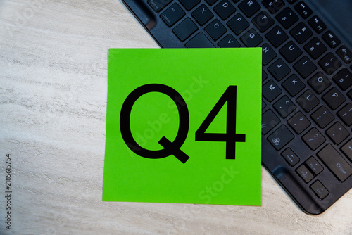 Q4 text on green sticky note placed on laptop keyboard on wooden office desk background. Fourth quarter business concept.