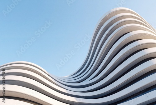 Modern architectural facade with curved white concrete layers against a clear blue sky