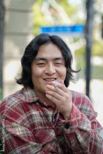 Photography A person smiles outdoors with one hand near the mouth and a cigarette visible