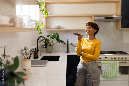 African American woman wearing mustard top talking into phone in kitchen by countertop, copy space