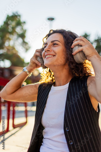The positive young woman enjoys the sound in the headphones in the city center. A happy woman enjoying the music walking through the city street.