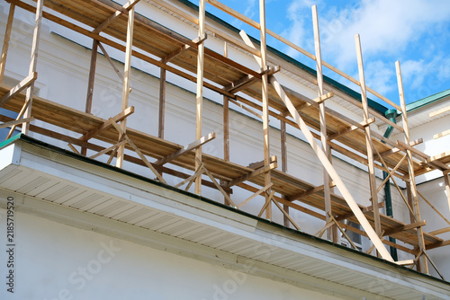 Bild auf Leinwand White building facade surrounded by wooden scaffolding during exterior construct
