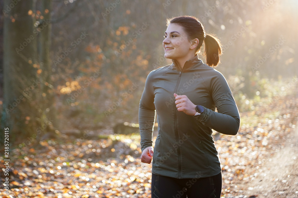 Fototapeta premium A young, cheerful, athletic woman in winter sportswear jogging, running and training outdoors on a early autumn morning