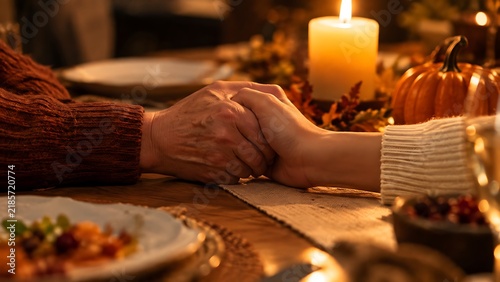 Close-up of two people holding hands across a Thanksgiving dinner table, with a lit candle and autumn decorations.