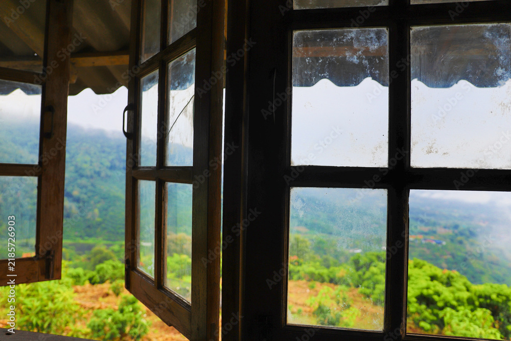Obraz premium View through open wooden windows overlooking mist covered green mountains and tropical hills.