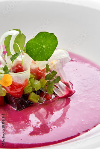 Macro extreme close-up of vibrant pink beetroot soup garnished with delicate microgreens, nasturtium leaf, and diced vegetables.