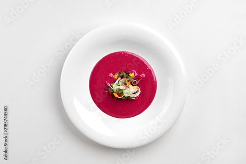 Gourmet pink beetroot cream soup served in a white bowl, garnished with microgreens and fresh herbs. Isolated on white background.