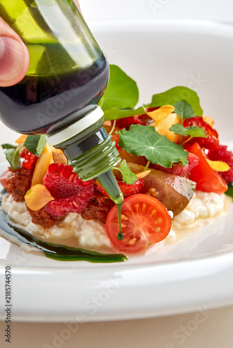 Chef dressing gourmet salad with green herb oil in white bowl, action macro shot.