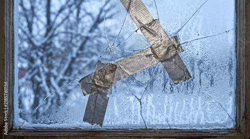 A close-up vector illustration showing a cracked single glass window pane temporarily held together by silver duct tape, covered in fine cold winter morning condensation droplets and frost textures.