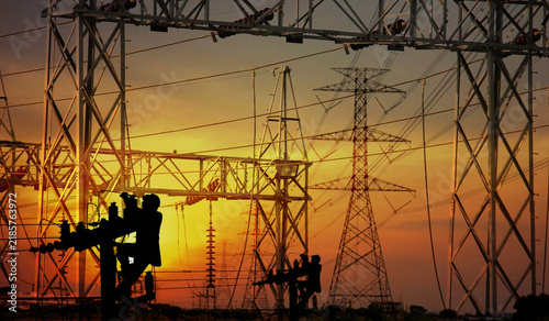 the electric workers working on pole overtime in front of group of object electric high electric pole steel structure in construction site on sunset abstract nature background