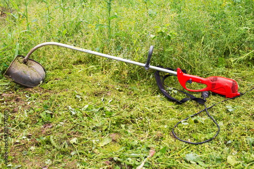 Electric string trimmer lying on cut grass