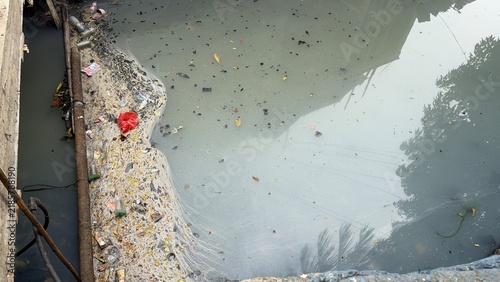 Fotografía Polluted dirty gray color stagnant river water with urban litter
