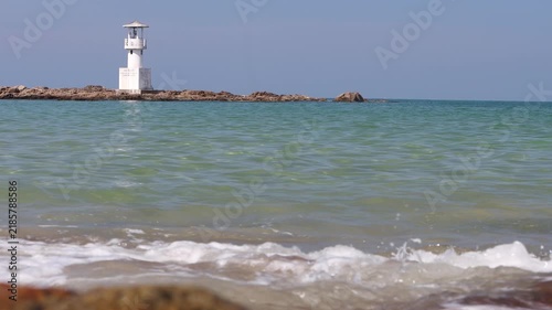 White Lighthouse on Rocky Outcrop Over Calm Turquoise Sea With Gentle Waves at Sunny Coast