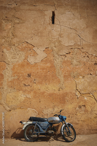 Fotografie Vintage blue moped parked against a cracked adobe wall