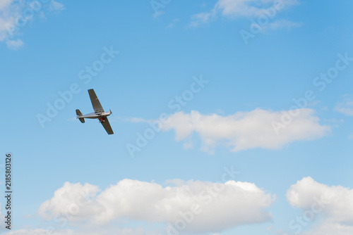 A small single-engine airplane banking in mid-air against a bright blue sky filled with white fluffy clouds, capturing a sense of freedom and flight.
