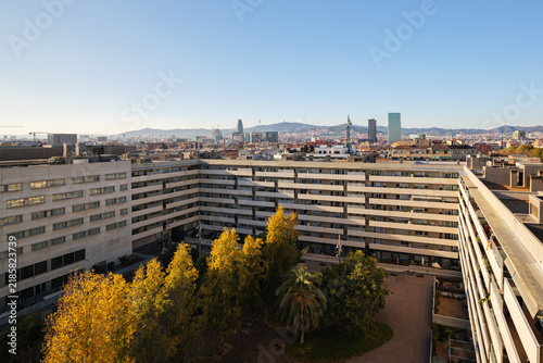 Aerial view modern residential district with landscaped courtyard trees, midrise buildings, clear blue sky, autumn foliage and distant urban skyline during daylight
