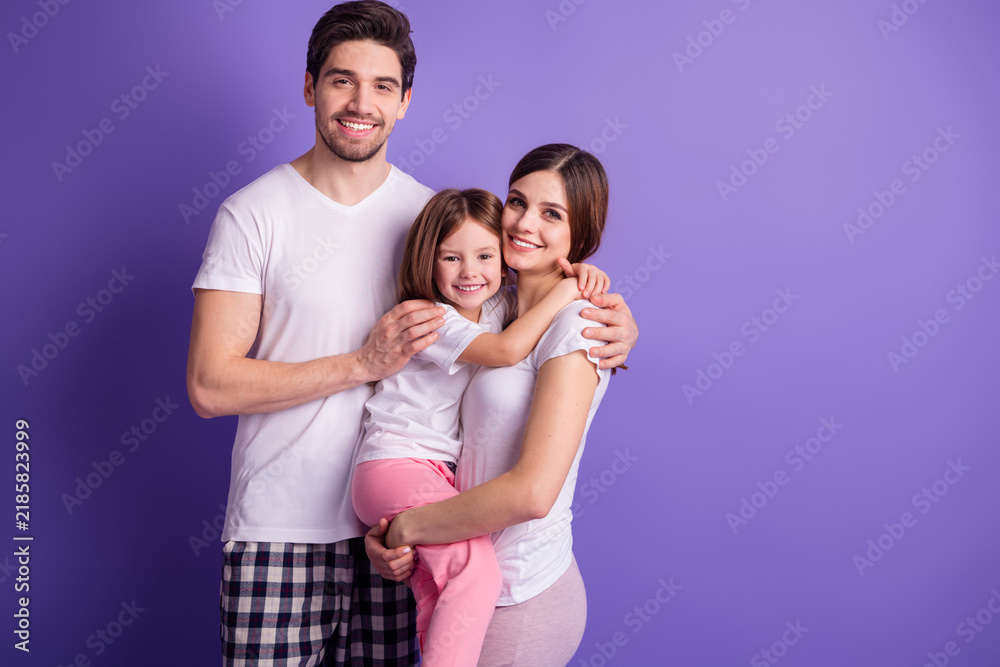 Fototapeta premium Happy young family embracing smiling parents holding daughter against purple background, casual home portrait conveying love and togetherness