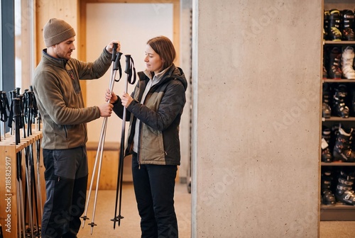 Happy Couple Choosing Winter Sports Poles at Rental Shop Counter