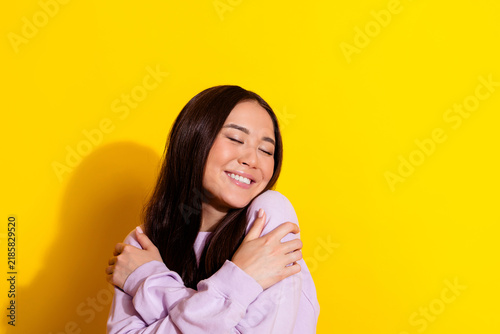 Fotografía Young woman hugging herself and smiling with eyes closed against a bright yellow