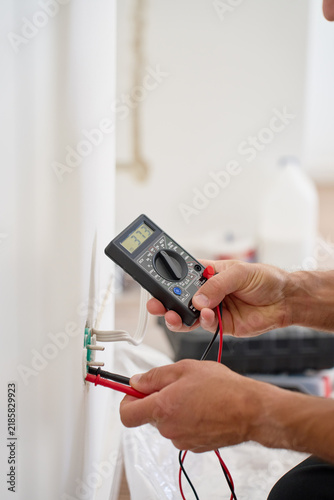 Plakat Electrician testing wall socket voltage with digital multimeter