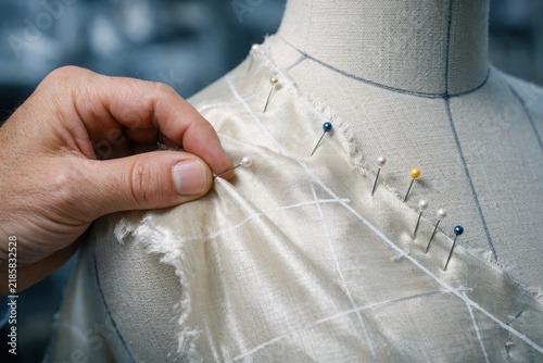 Closeup shows craftsman fitting muslin fabric on dress form with pins