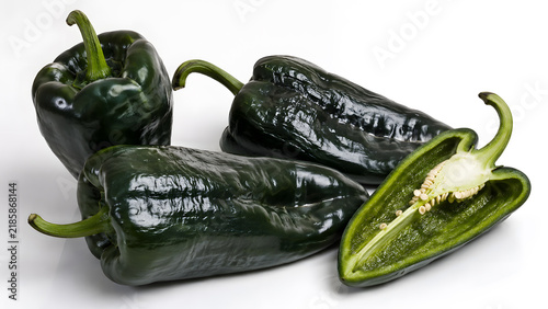 Dark green glossy poblano peppers with one piece cut vertically in half displaying seeds isolated on white background