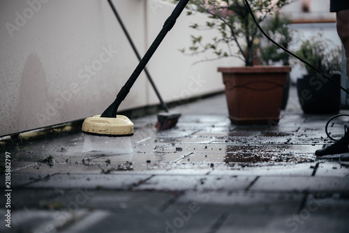 Man pressure washing dirty patio tiles with a power washer outdoors, removing moss and grime from residential walkway, home maintenance, exterior cleaning, DIY renovation