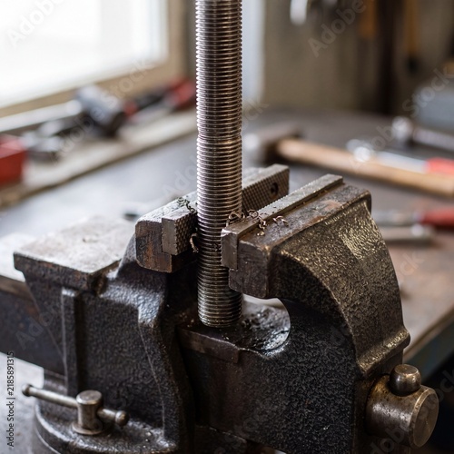 Threaded metal rod clamped in heavy duty bench vise in workshop