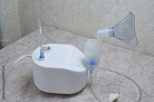 Fully assembled white compressor nebulizer with connected tubing, medicine chamber, and plastic mask resting on a patterned table. Respiratory therapy, asthma treatment, and home care concept