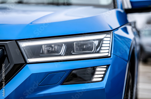 Close-up eye level shot of modern luxury blue car LED headlight and front bumper, featuring sharp automotive lines, metallic finish, advanced technology, speed, and premium vehicle design.
